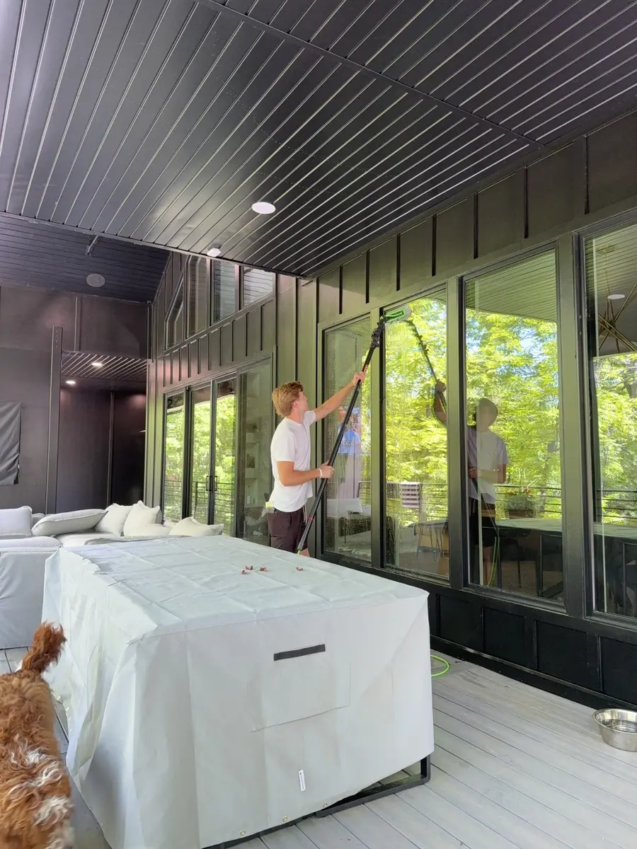 Luma Solutions technician cleaning tall glass walls at a modern Northwest Arkansas home
